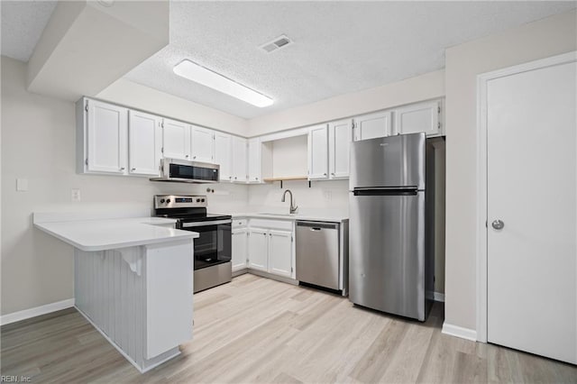 kitchen with a peninsula, stainless steel appliances, visible vents, and light wood-style floors
