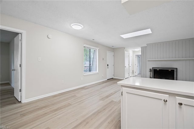 kitchen featuring light wood finished floors, light countertops, a skylight, a fireplace, and open floor plan
