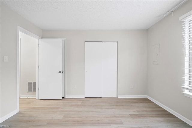 unfurnished bedroom with a textured ceiling, light wood-style flooring, visible vents, and baseboards