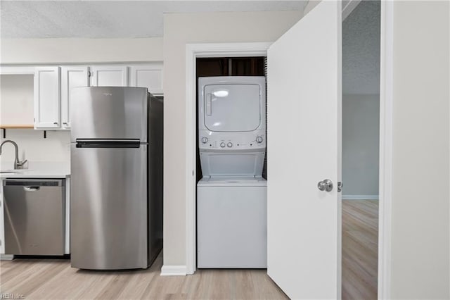 laundry room with light wood finished floors, a sink, baseboards, stacked washing maching and dryer, and laundry area