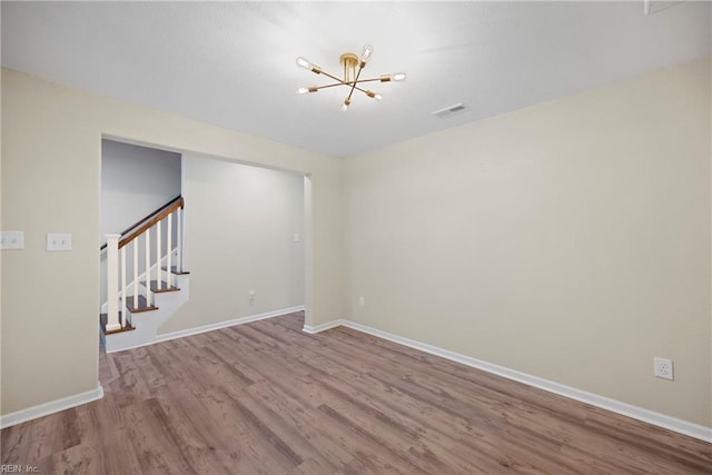empty room featuring wood finished floors, baseboards, and a notable chandelier