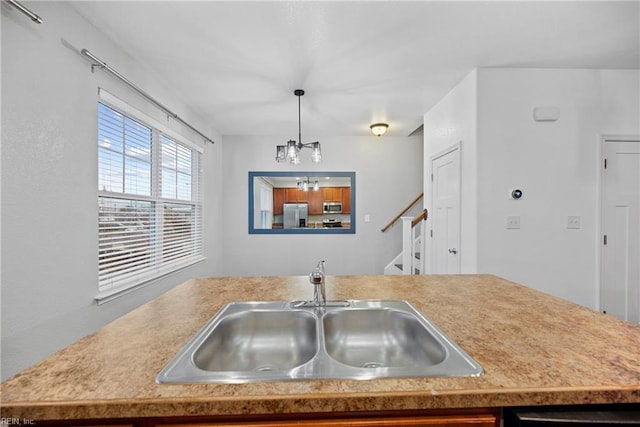 kitchen with a sink, an inviting chandelier, pendant lighting, light countertops, and appliances with stainless steel finishes