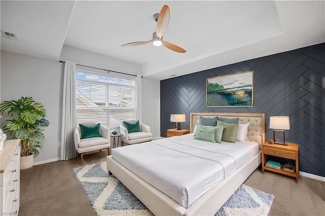 bedroom featuring visible vents, a ceiling fan, an accent wall, baseboards, and carpet flooring