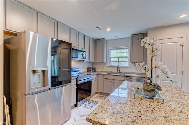 kitchen with light stone counters, a sink, gray cabinets, appliances with stainless steel finishes, and visible vents