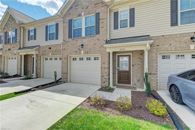 townhome / multi-family property with a garage, driveway, and brick siding