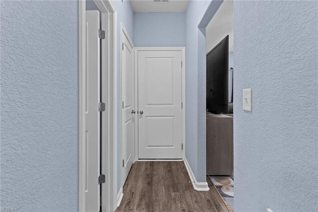 corridor featuring a textured wall, baseboards, visible vents, and dark wood-style flooring