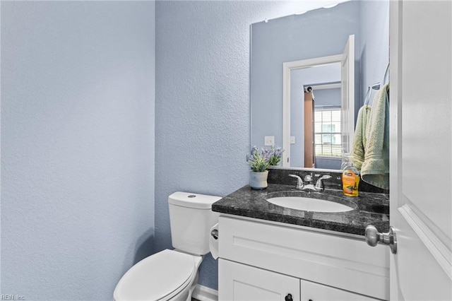bathroom with a textured wall, vanity, and toilet