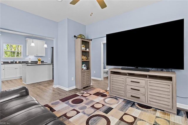living area with baseboards, a ceiling fan, and light wood-style floors