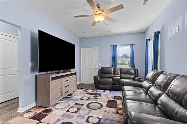 living room featuring light wood-style flooring, visible vents, a ceiling fan, and baseboards