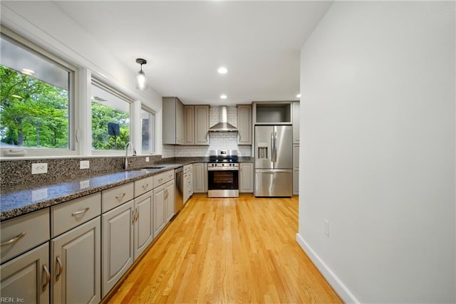 kitchen featuring a sink, decorative backsplash, light wood-type flooring, stainless steel appliances, and wall chimney exhaust hood