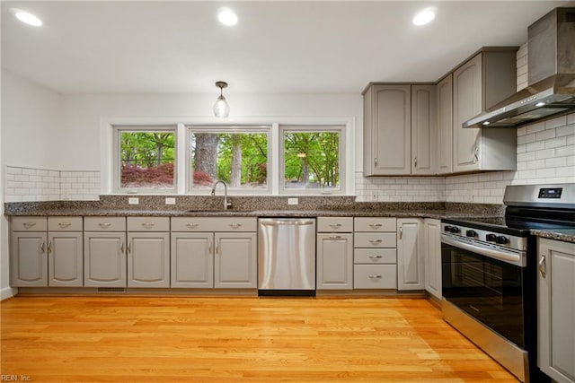 kitchen with stainless steel appliances, a sink, wall chimney exhaust hood, decorative backsplash, and light wood-style flooring