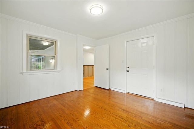 interior space featuring a baseboard heating unit, a decorative wall, crown molding, and wood finished floors