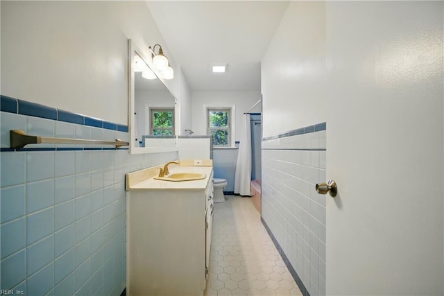 bathroom featuring tile patterned flooring, toilet, vanity, tile walls, and wainscoting