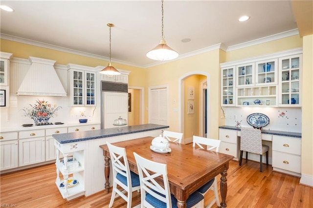 dining area featuring arched walkways, light wood-type flooring, crown molding, and built in desk
