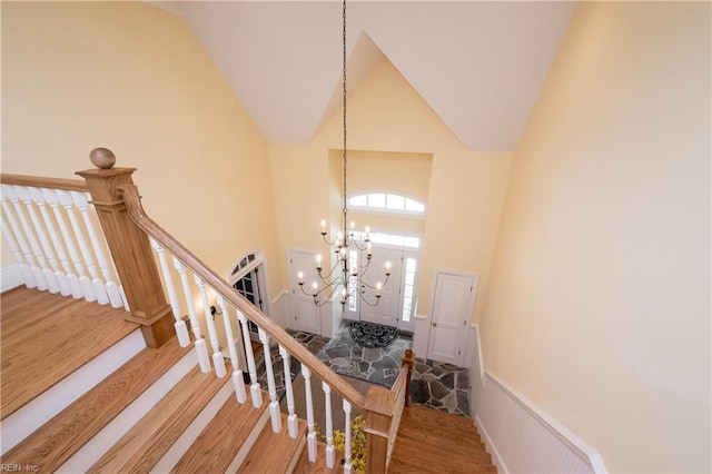 staircase with high vaulted ceiling, an inviting chandelier, and wood finished floors