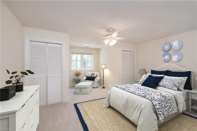 bedroom featuring light carpet, two closets, and ceiling fan