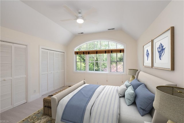 carpeted bedroom featuring baseboards, visible vents, lofted ceiling, ceiling fan, and two closets