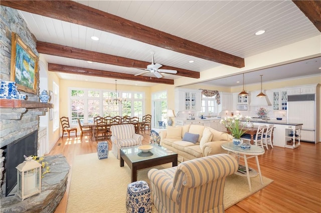 living room featuring light wood-style flooring, a healthy amount of sunlight, a stone fireplace, and ceiling fan with notable chandelier