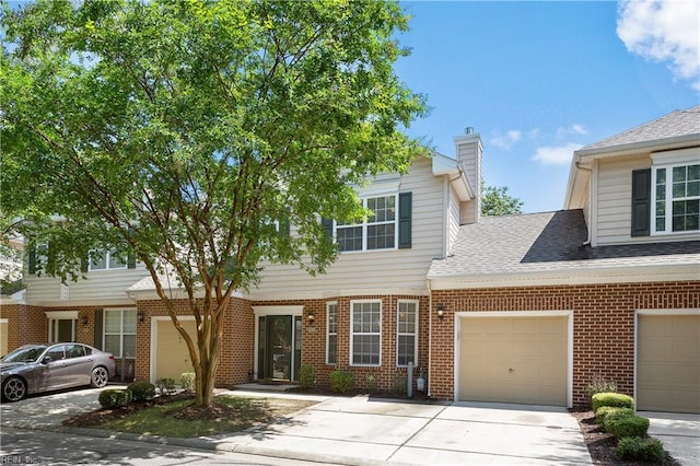 townhome / multi-family property with brick siding, a chimney, a garage, and concrete driveway