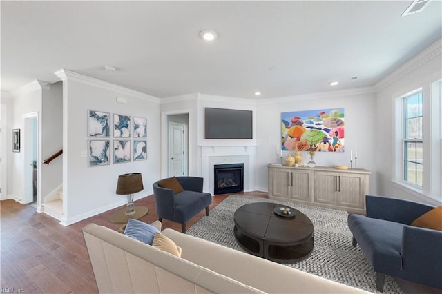 living area with a glass covered fireplace, wood finished floors, baseboards, and crown molding