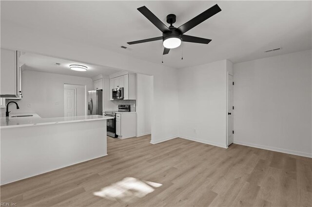 unfurnished living room featuring a ceiling fan, a sink, light wood finished floors, baseboards, and visible vents