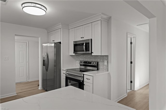 kitchen featuring stainless steel appliances, light wood-style flooring, tasteful backsplash, baseboards, and light stone countertops
