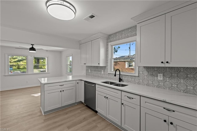 kitchen featuring dishwasher, a sink, light wood-type flooring, a peninsula, and tasteful backsplash