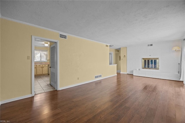 unfurnished living room with a textured ceiling, wood finished floors, visible vents, and baseboards