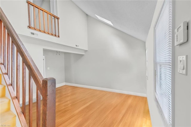 stairs featuring high vaulted ceiling, wood finished floors, a skylight, baseboards, and visible vents
