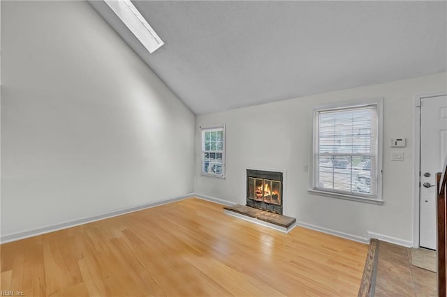 unfurnished living room with vaulted ceiling with skylight, wood finished floors, a glass covered fireplace, and baseboards