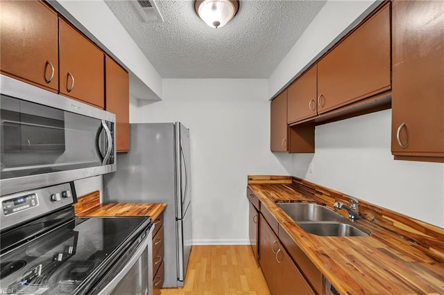 kitchen with a sink, wooden counters, light wood-style floors, baseboards, and appliances with stainless steel finishes