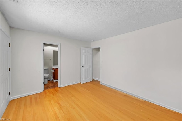 unfurnished bedroom with light wood-type flooring, ensuite bathroom, baseboards, and a textured ceiling