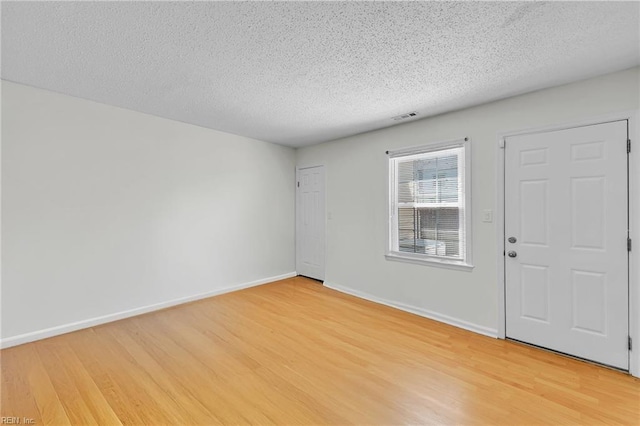 interior space featuring visible vents, baseboards, a textured ceiling, and light wood-style floors
