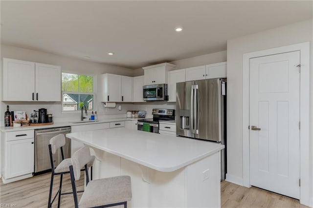kitchen with white cabinets, stainless steel appliances, a sink, light wood-style floors, and light countertops