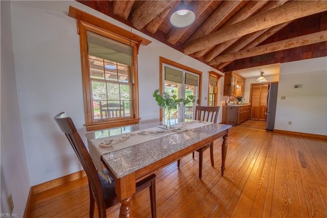 dining room with lofted ceiling with beams, baseboards, and light wood-style floors