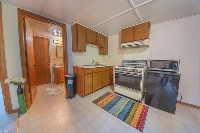 kitchen with brown cabinets, under cabinet range hood, white gas range, stainless steel microwave, and refrigerator