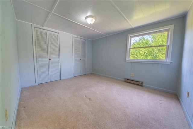 unfurnished bedroom with multiple closets, carpet, and a baseboard radiator