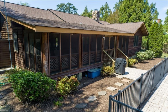 exterior space featuring a chimney, roof with shingles, and a sunroom