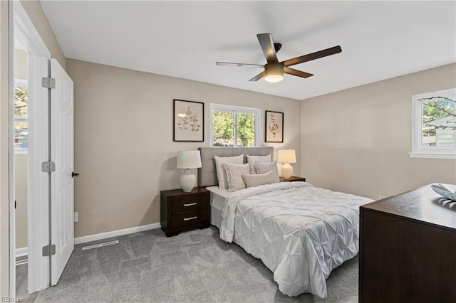 bedroom with ceiling fan, light carpet, multiple windows, and baseboards