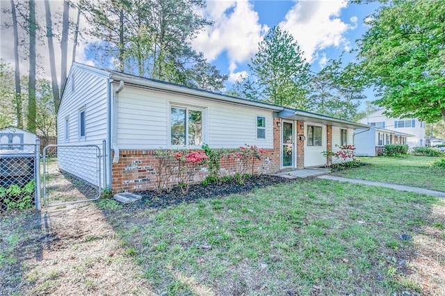 ranch-style home featuring a gate, a front lawn, fence, brick siding, and a storage unit