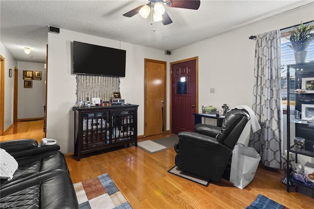 living area featuring light wood finished floors, a textured ceiling, and a ceiling fan