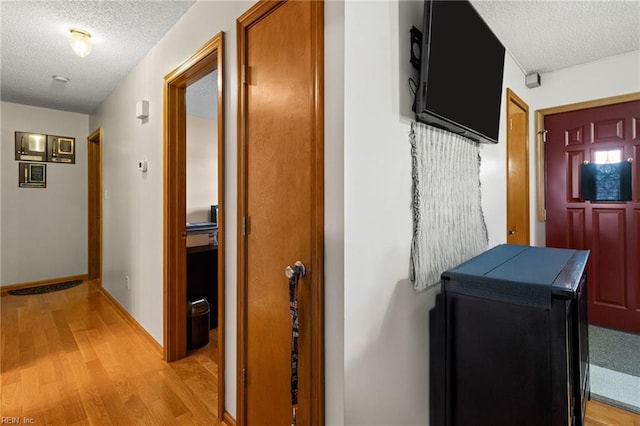 hallway with light wood-type flooring and a textured ceiling