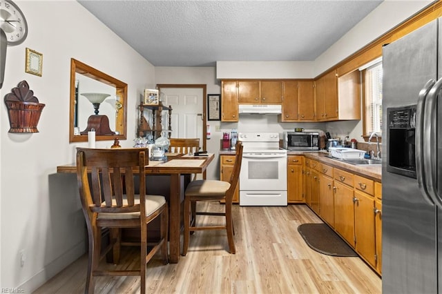 kitchen with light wood-style flooring, a sink, brown cabinets, under cabinet range hood, and appliances with stainless steel finishes