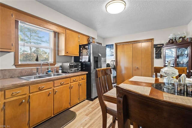 kitchen with stainless steel fridge with ice dispenser, brown cabinetry, a sink, light wood-style flooring, and a textured ceiling