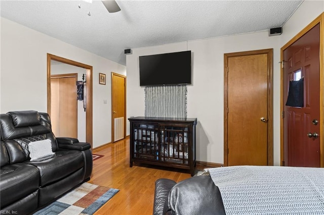 bedroom with a textured ceiling, light wood-type flooring, visible vents, and ceiling fan