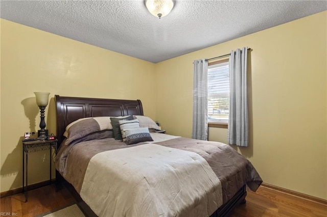 bedroom with baseboards, wood finished floors, and a textured ceiling