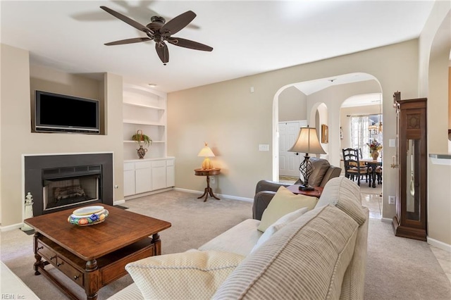 living area with arched walkways, baseboards, light colored carpet, and ceiling fan