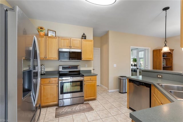 kitchen featuring dark countertops, a sink, light tile patterned floors, stainless steel appliances, and decorative light fixtures