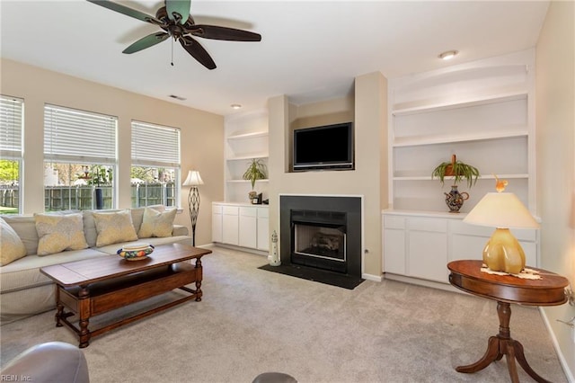 living room featuring a fireplace with flush hearth, ceiling fan, built in shelves, light colored carpet, and visible vents