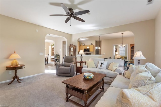 carpeted living area featuring baseboards, arched walkways, visible vents, and ceiling fan with notable chandelier